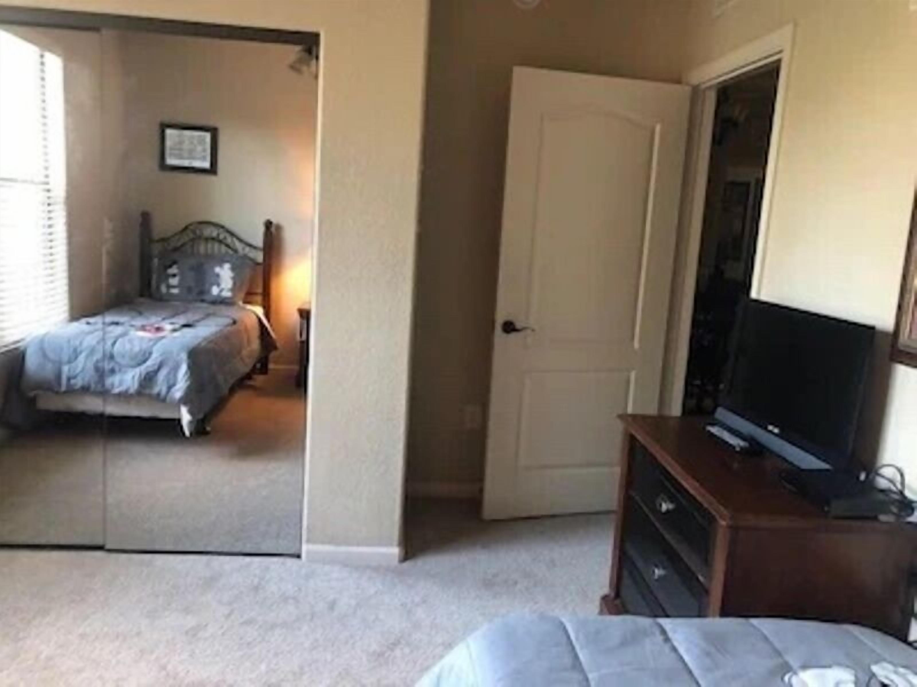 A bedroom with a bed, a television on a stand, and a door leading to another room.