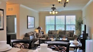 A cozy living room with a sofa, chairs, a coffee table, and a dining table set for two. - Pool view condo minutes to Disney World (Davenport)