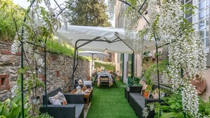 An outdoor patio with a table and chairs, a green artificial turf floor, and white flowering plants.