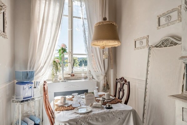 Et værelse med et bord dækket til måltid, et vindue med gardiner og en lampe.