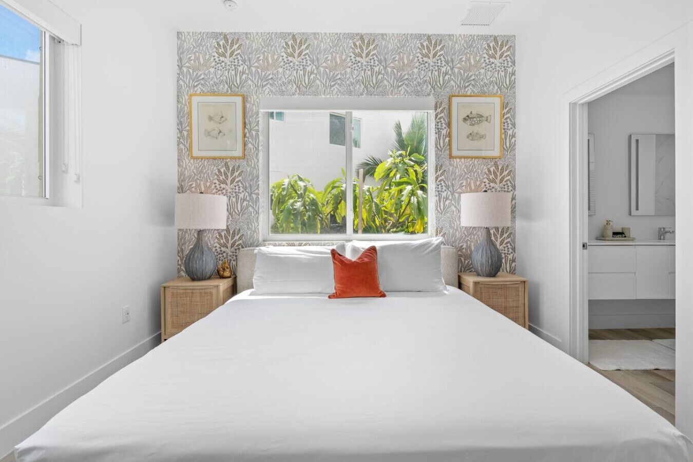 Een ruime slaapkamer met een groot bed, twee nachtkastjes met lampen, een raam met uitzicht op groen en een badkamer die zichtbaar is door een geopende deur.