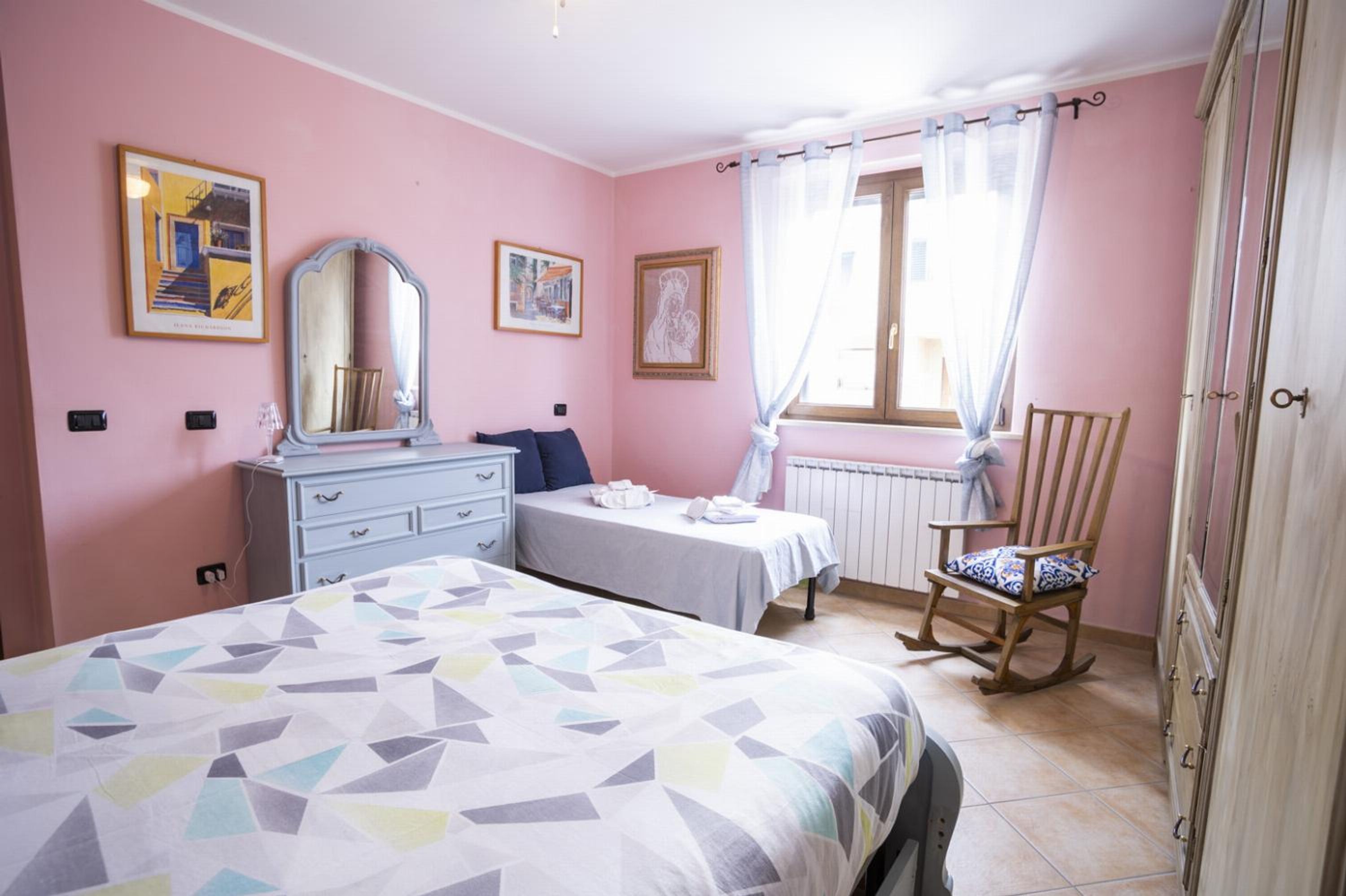 A bedroom with a bed, a dresser, a chair, and a window with curtains.