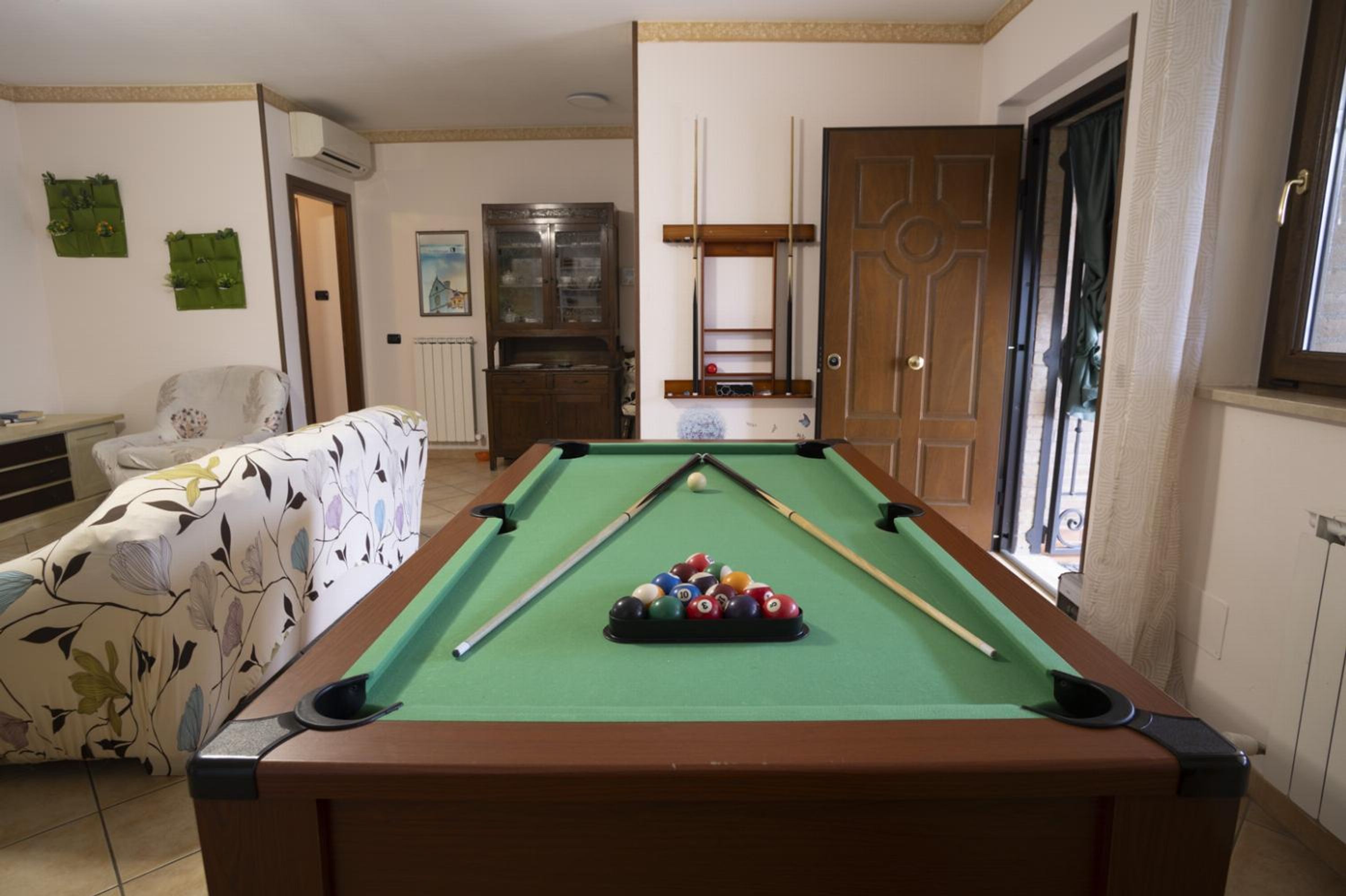 A pool table in a room with a sofa, a cabinet, and a door.