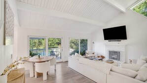 Un vaste salon avec un canapé blanc, une table à manger avec des chaises, une cheminée et un téléviseur fixé au mur.