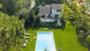 Vue aérienne d’une maison avec une piscine, entourée d’une pelouse bien entretenue et d’arbres.