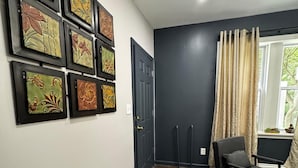 Een kamer met een donkergrijze deur, een zwarte stoel en een muur versierd met ingelijste bloemkunst.