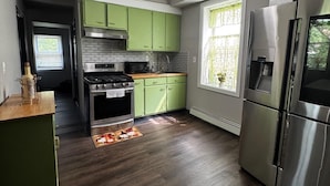 Een moderne keuken met groene kastjes, roestvrijstalen apparatuur en een donker houten vloer.