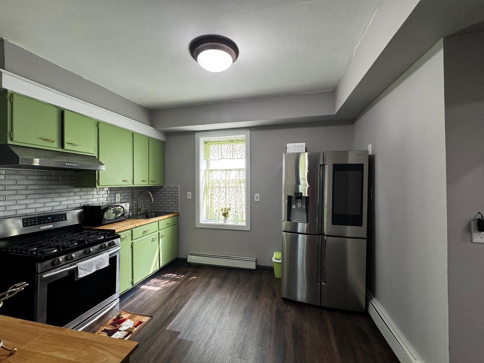 A compact kitchen with green cabinets, a stainless steel refrigerator, and a built-in oven.