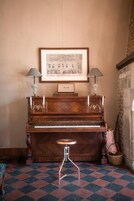 Un piano de cola con un cuadro enmarcado encima, dos lámparas a cada lado y un taburete pequeño al frente.