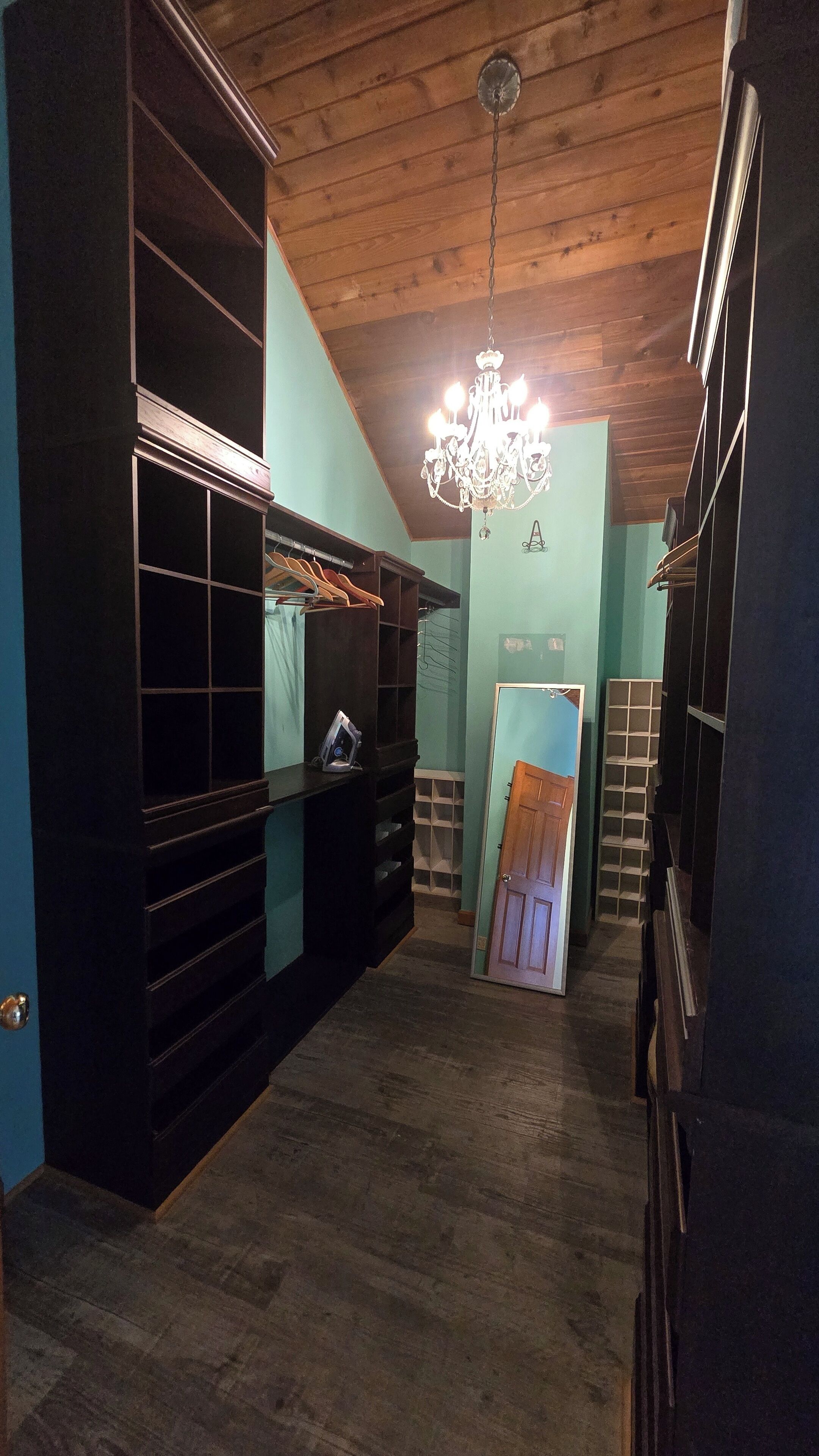 A room with a wooden ceiling, a chandelier, and built-in shelving units.
