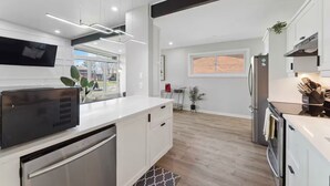 Una cocina moderna con armarios blancos, horno empotrado y refrigerador de acero inoxidable.