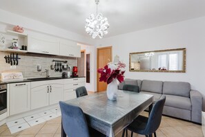 Een moderne keuken met witte kasten, een eettafel met stoelen, een vaas met bloemen, een bank en een grote spiegel aan de muur.