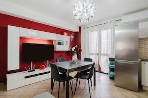 Una cocina moderna con refrigerador empotrado, una mesa de comedor con sillas, un televisor de pantalla plana y un jarrón decorativo.