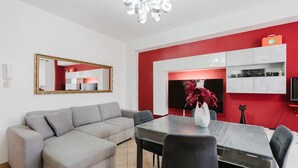 A modern living room with a grey sofa, a dining table with chairs, a chandelier, a red accent wall, a white cabinet with shelves, and a black cat statue. - Casa Luna with Private Terrace, Wi-Fi and Air Conditioning (Balestrate)