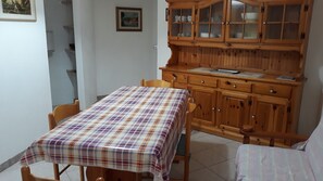 A dining area with a table covered by a plaid tablecloth, wooden cabinets with glass doors, and a chair.