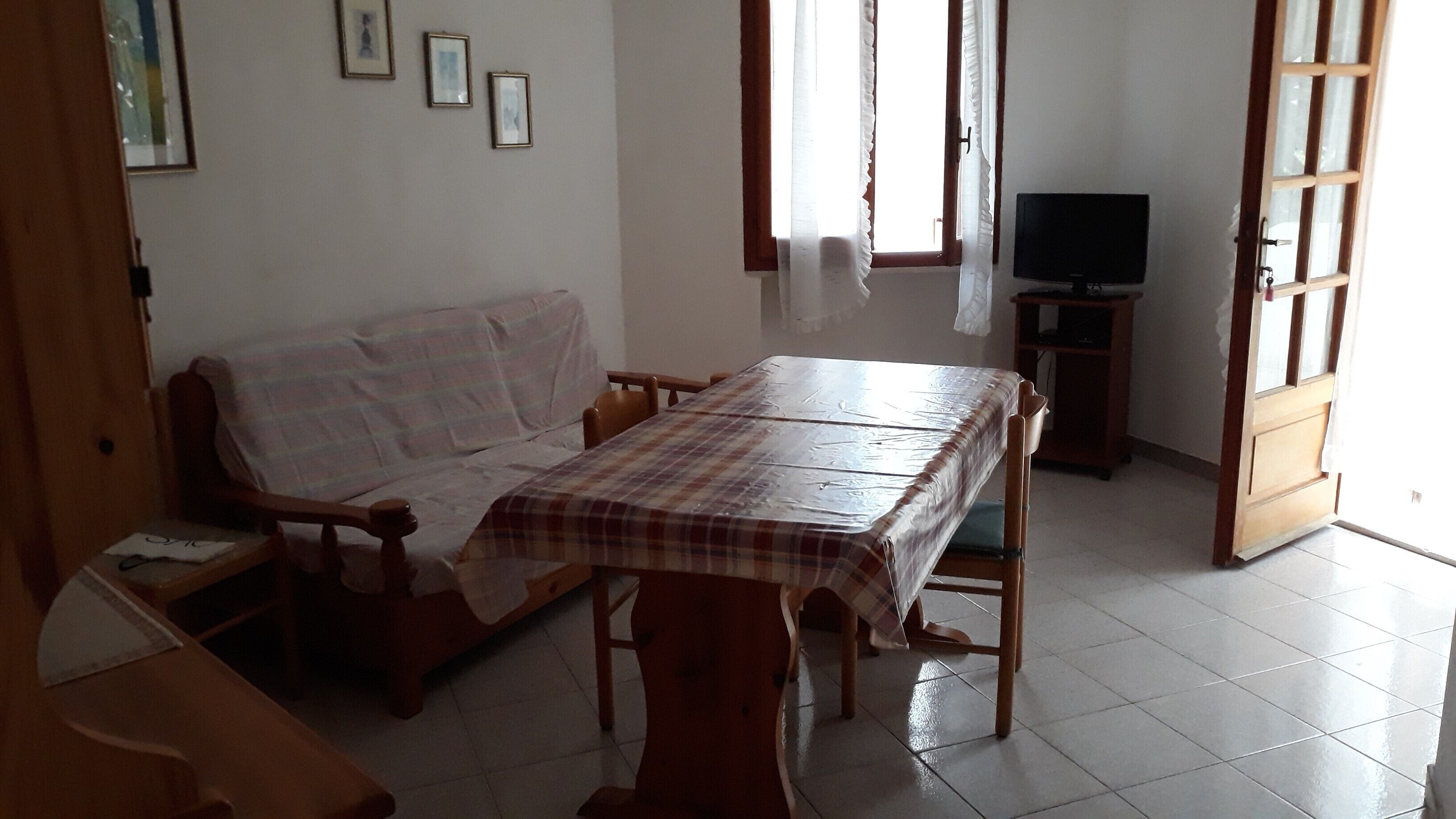A room with a sofa, a table with a tablecloth, a television on a stand, and a door.