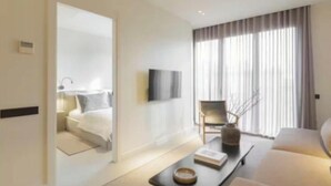 Una habitación de hotel moderna con una cama, un televisor de pantalla plana montado en la pared, un sofá, una mesa de centro y un amplio ventanal con cortinas.