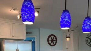 Eine moderne Küche mit einem Edelstahlkühlschrank, einem schwarzen Induktionskochfeld und blauen Pendelleuchten.