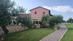 A pathway leading to a building with a stone wall and greenery.