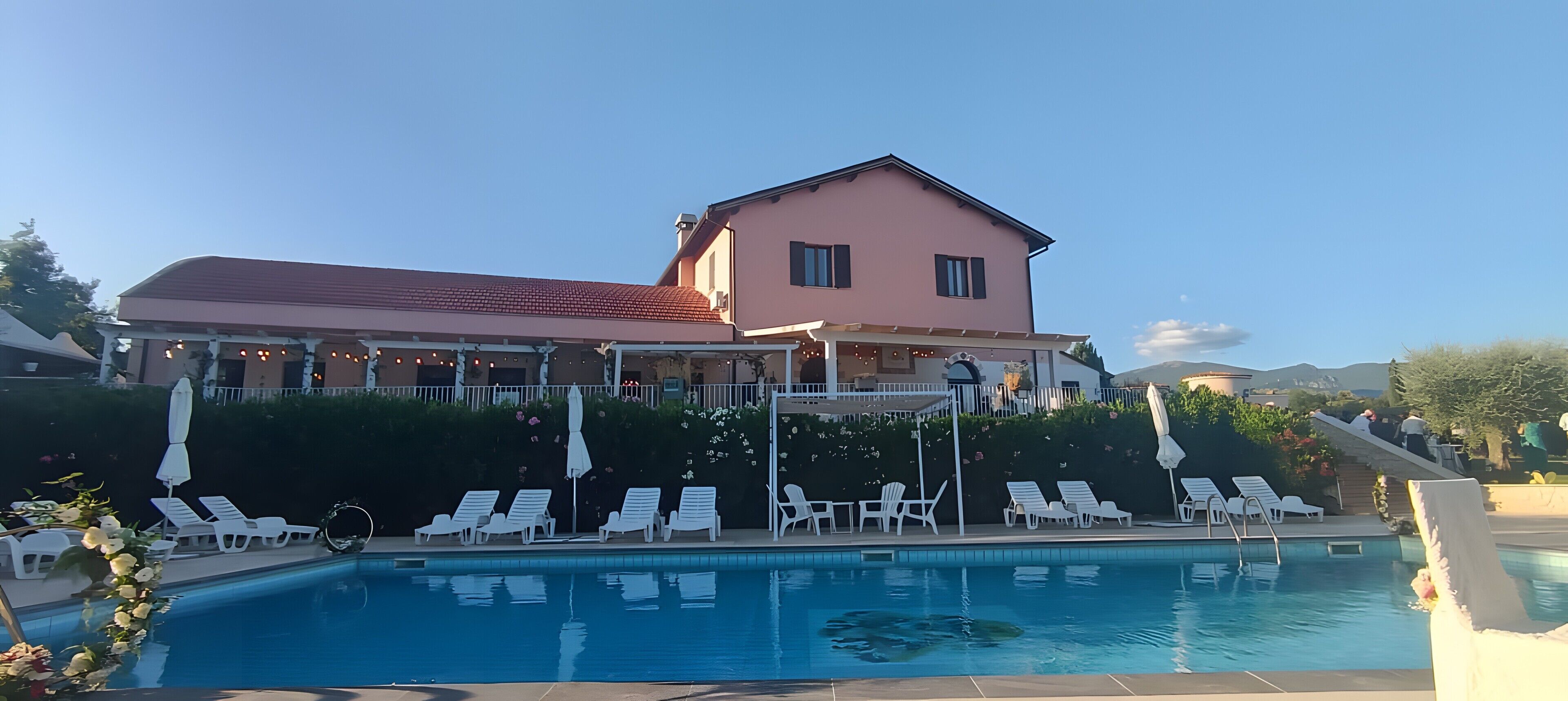 A large building with a swimming pool, white lounge chairs, and a covered patio area.
