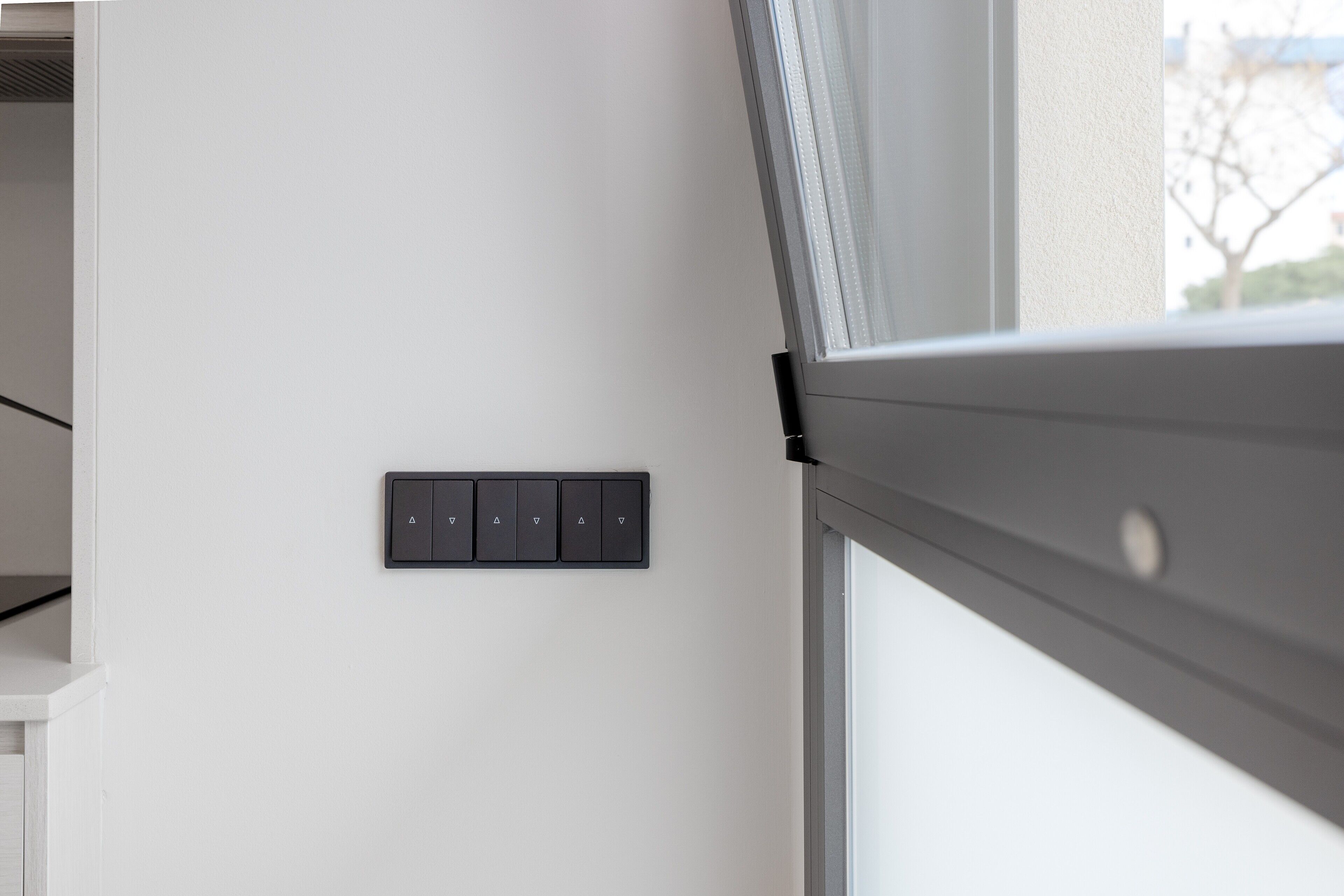 Una habitación moderna con una pared blanca, un ventanal con vistas y un panel de control montado en la pared.