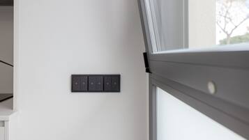 Una habitación moderna con una pared blanca, un ventanal con vistas y un panel de control montado en la pared.