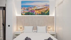 Een hotelkamer met een bed, twee nachtkastjes, een stadsgezichtschilderij en handdoeken op het bed.
