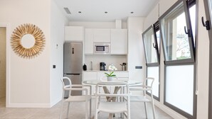 Een moderne keuken met witte kastjes, een ingebouwde magnetron en een eetgedeelte met een glazen tafel en witte stoelen.