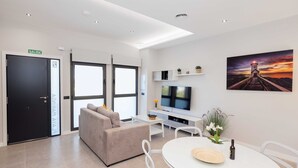 Een moderne hotelkamer met een bank, een eettafel, een televisie en een schilderij van een vuurtoren.