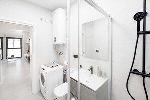 Une salle de bain moderne équipée d’un lave-linge, de toilettes, d’un lavabo et d’une douche.