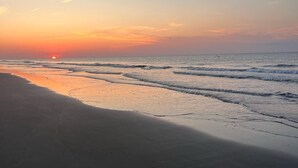 Ein Strand bei Sonnenuntergang, sanfte Wellen umspülen das Ufer.