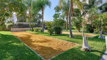 Un patio con una cancha de arena, rodeado de césped y palmeras.