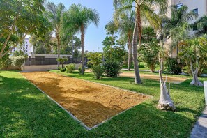 Un patio con una cancha de arena, rodeado de césped y palmeras.