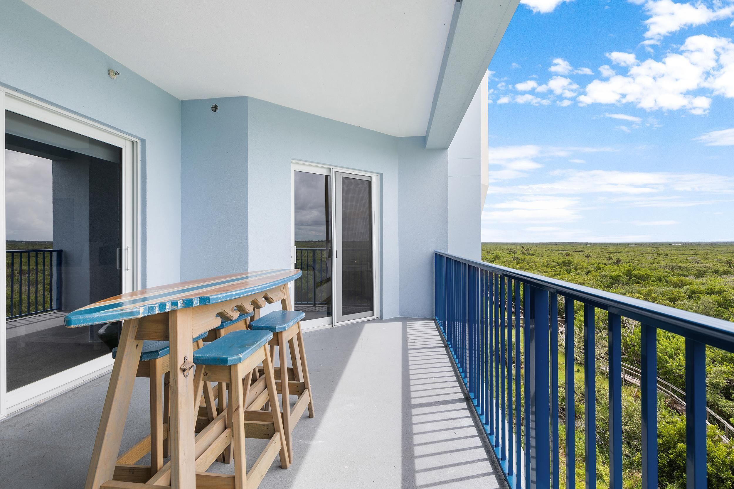 Ein Balkon mit Holztisch und -stühlen, einem blauen Geländer und Blick auf eine grüne Landschaft.