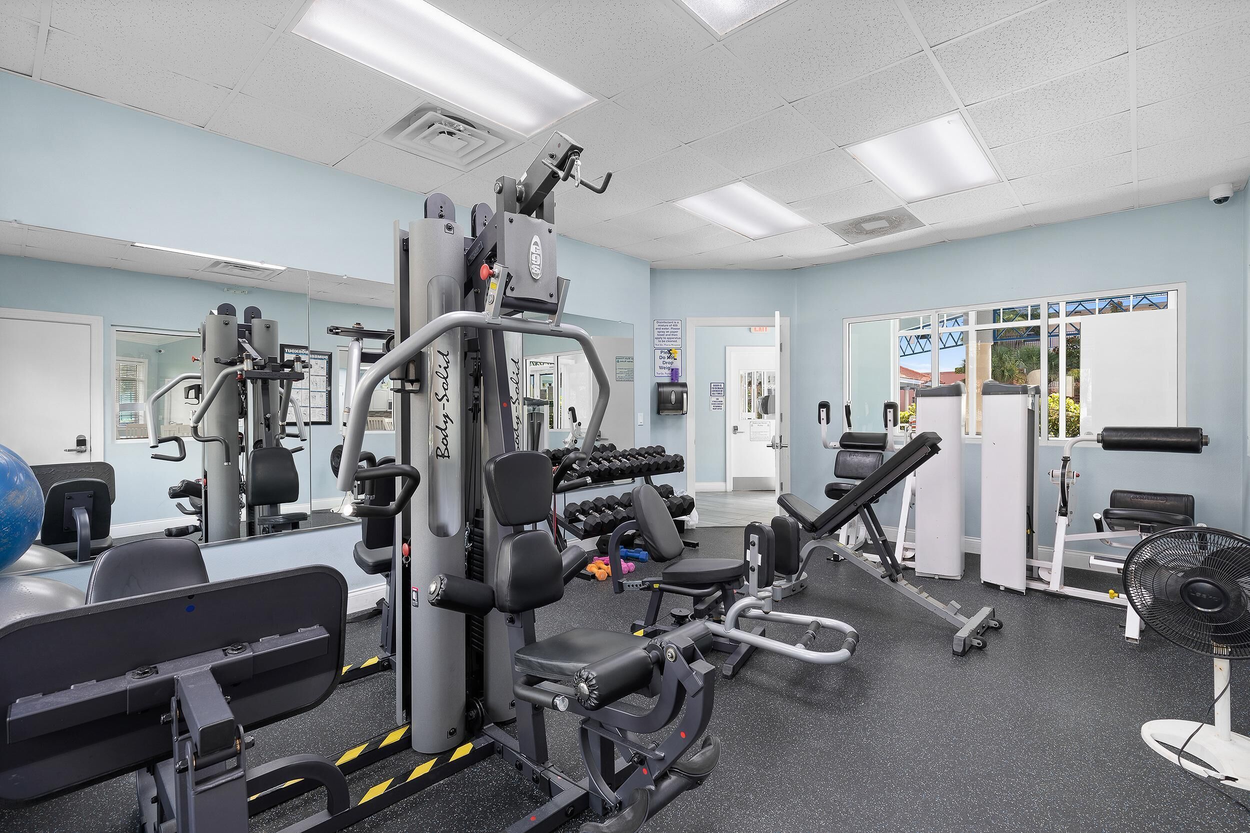 A gym with various exercise machines, a mirror, and a door leading outside.