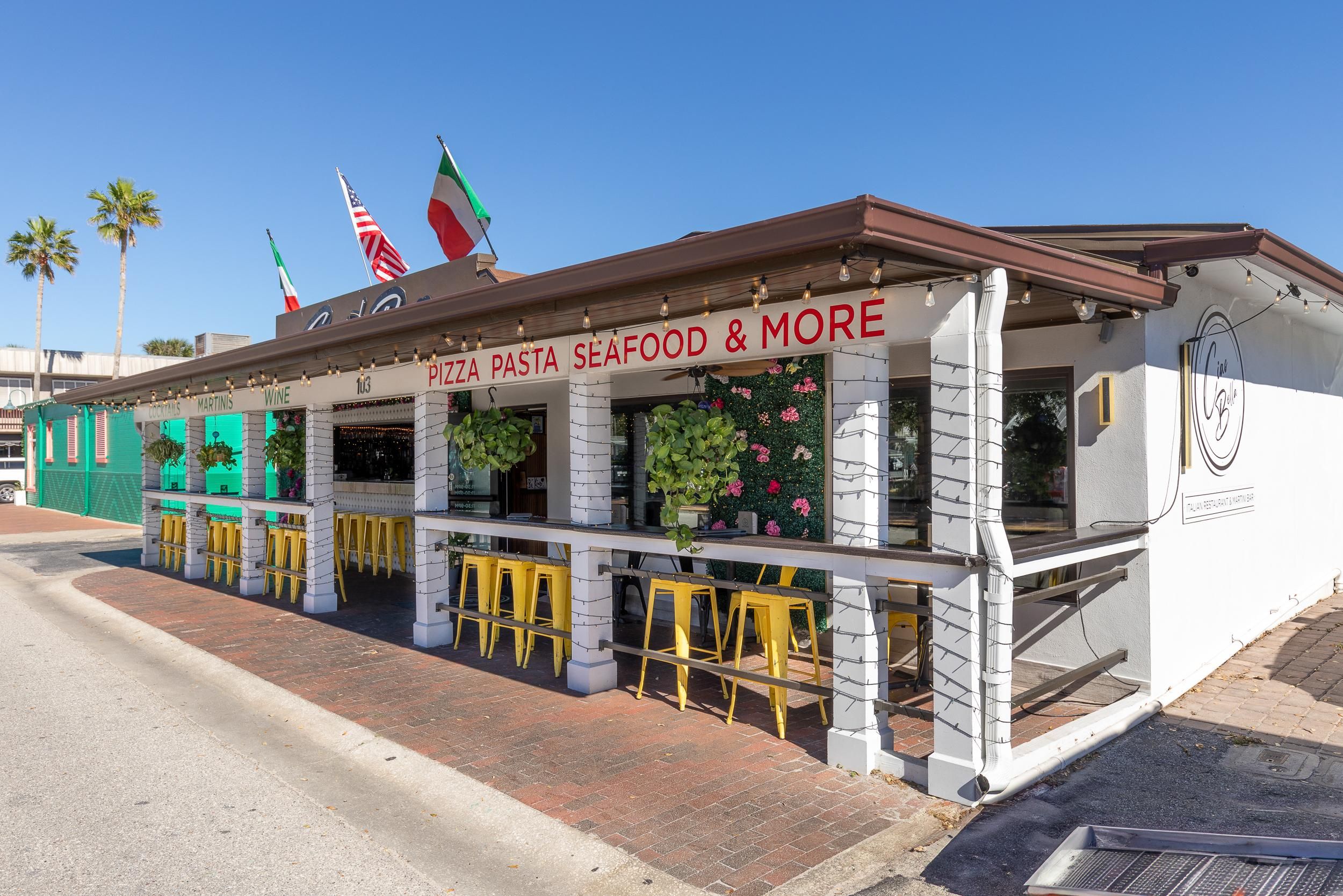 Een restaurant aan zee met een bord waarop 'PIZZA PASTA ZEEVOEDSEL & MEER' staat.