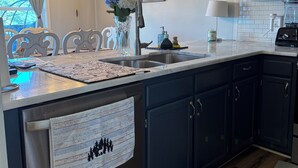A modern kitchen with dark cabinets, a stainless steel sink, and a hanging light fixture. - Relaxing Mountain Escape—Steps to Town, Minutes to Slopes (Beech Mountain)