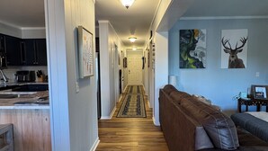 A modern kitchen with dark cabinets, a wooden countertop, and a built-in oven. A hallway with a patterned rug leads to a living area with a brown leather sofa and a coffee table. - Relaxing Mountain Escape—Steps to Town, Minutes to Slopes (Beech Mountain)