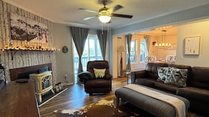 A cozy living room with a fireplace, a leather armchair, a sofa, and a dining area with a chandelier. - Relaxing Mountain Escape—Steps to Town, Minutes to Slopes (Beech Mountain)
