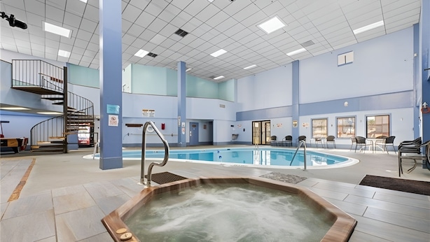 A large indoor swimming pool with a hot tub, surrounded by seating areas and a staircase. - Relaxing Mountain Escape—Steps to Town, Minutes to Slopes (Beech Mountain)