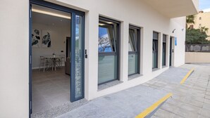 Un edificio moderno con entrada por puerta de vidrio, un área de comedor con sillas y una mesa, y vista despejada al cielo.
