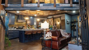 A spacious loft with a kitchen, dining area, and living room. It features a high ceiling, exposed beams, and a staircase leading to an upper level.