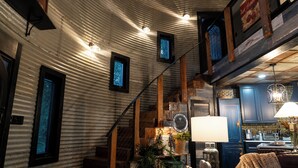 A rustic interior with exposed wooden beams, a staircase, a kitchen area, and a dining space.