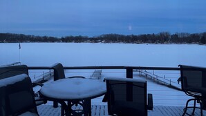 A snow-covered deck with outdoor seating and a view of a frozen lake.