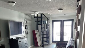 A living room with a TV, a sofa, a staircase, and a door leading outside.