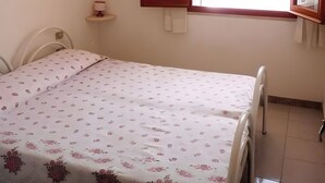Una stanza con un letto, una finestra con tende, un lampadario e un piccolo ripiano.