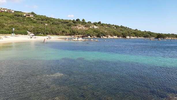 Una spiaggia costiera con acque limpide, litorale sabbioso e edifici su una collina.