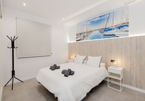 A hotel room with a bed, a nightstand, a coat rack, and a large wall mural of a marina.
