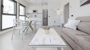 Un salon moderne avec une table basse en verre, un canapé beige et un coin repas avec des chaises blanches.
