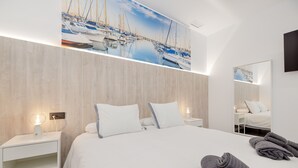 Une chambre d’hôtel moderne avec un grand lit, une table de chevet, un miroir fixé au mur et un tableau représentant des bateaux.